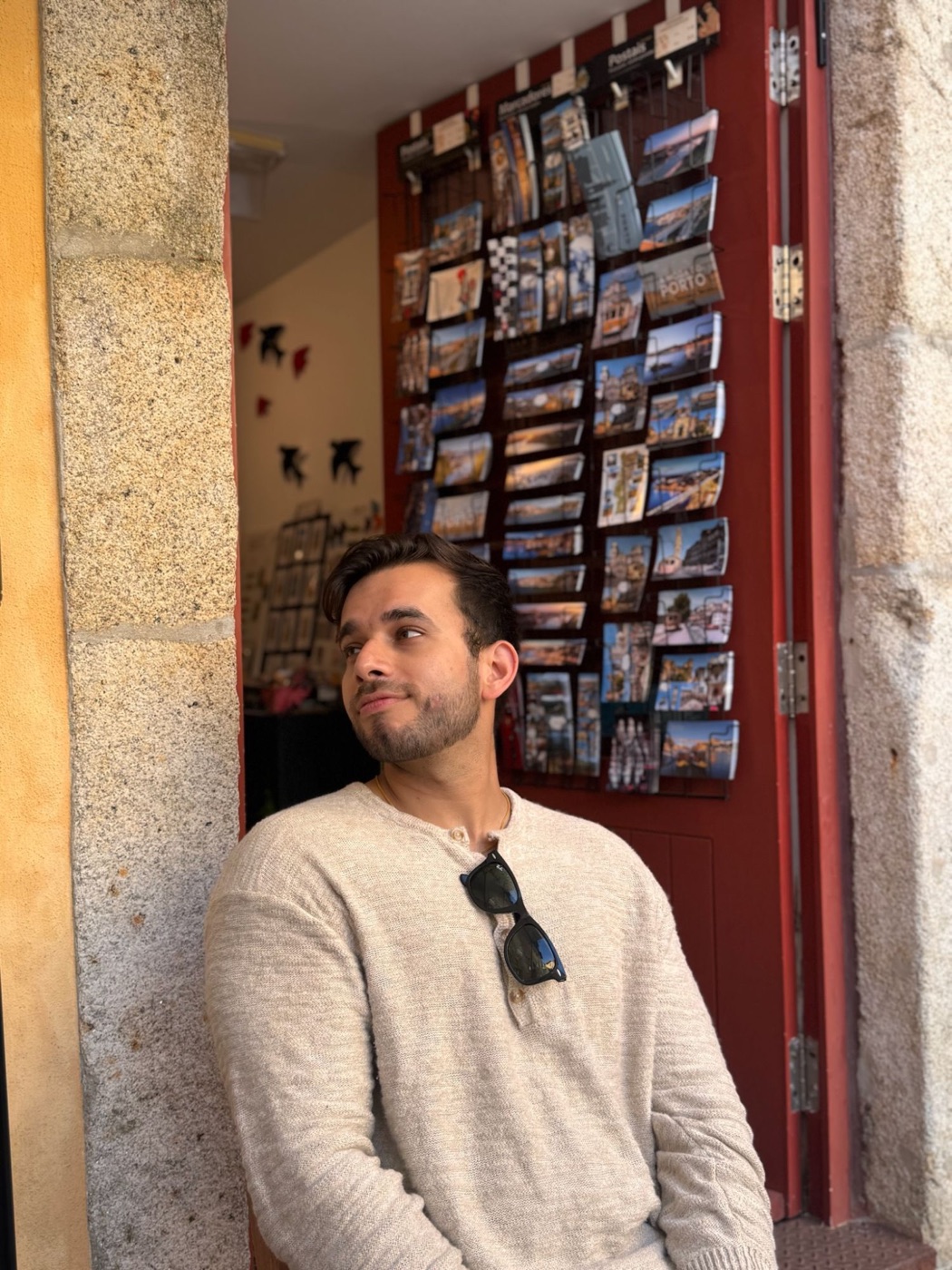 Anam leaning in a doorway in front of a postcard rack in Porto